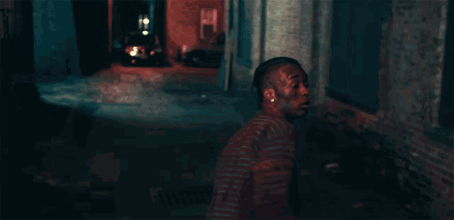 a man walking down a dark alleyway with a car parked behind him