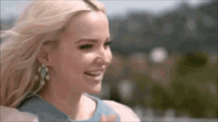a blonde woman wearing a blue dress and earrings smiles for the camera