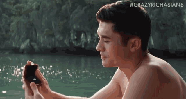 a shirtless man is holding a ring in his hand while sitting on the beach .