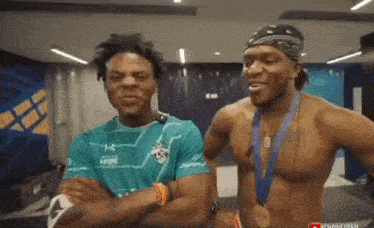 a shirtless man with a medal around his neck is standing next to another shirtless man with a bandana on his head .