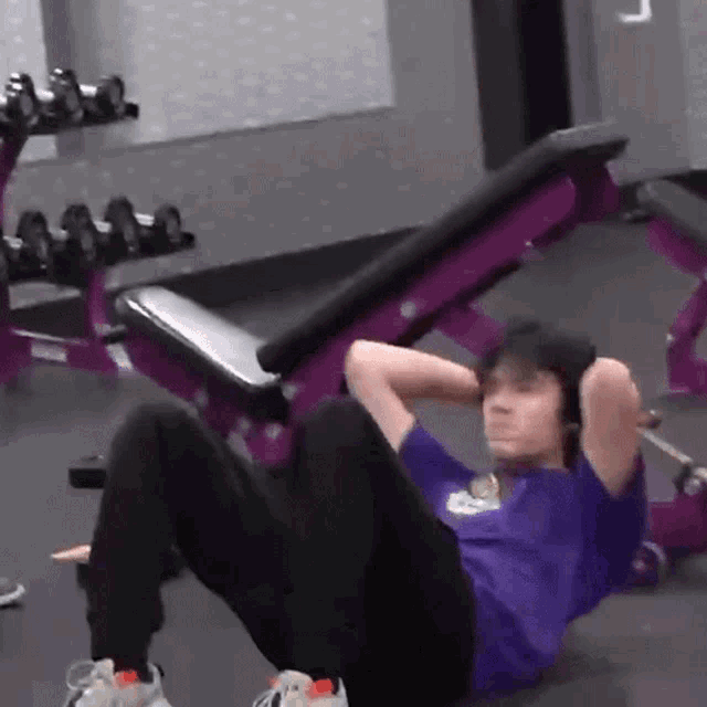 a man in a purple shirt is doing sit ups on a purple bench