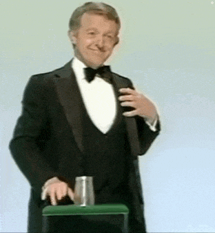 a man in a tuxedo and bow tie is standing next to a green stool .