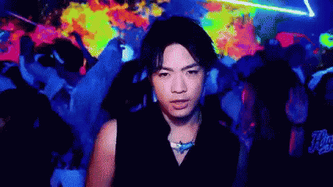 a man in a black shirt is standing in front of a crowd of people in a club .