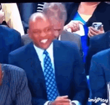 a man in a suit and tie is sitting in a crowd with his tongue out