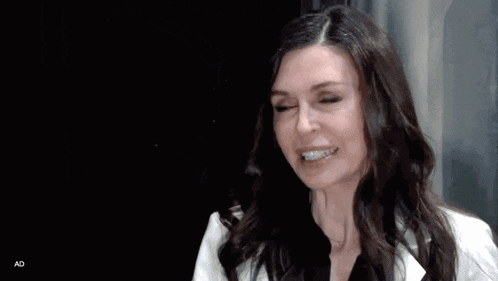 a woman with long dark hair is wearing a white jacket and black shirt and smiling .