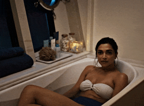 a woman is laying in a bathtub with a tray of candles on the window sill