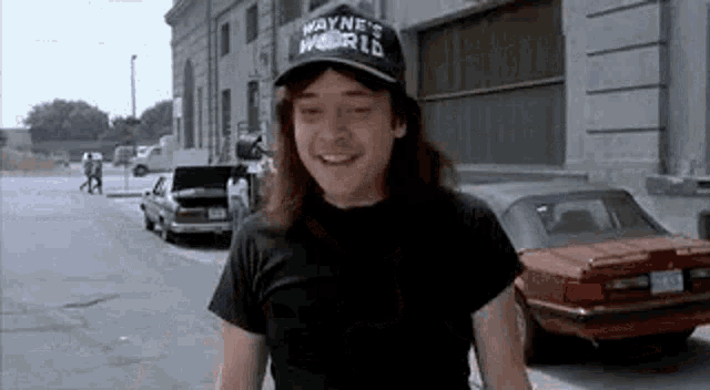 a man wearing a wayne 's world hat and a black shirt is walking down the street .
