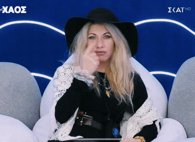 a woman wearing a black hat and a white scarf is sitting in a chair on a screen that says kaos