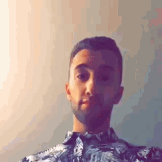 a man with a beard wearing a floral shirt is taking a selfie .
