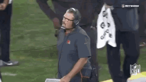 a man wearing headphones and glasses stands on a football field .