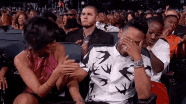 a man is covering his face with his hand while a woman applauds him