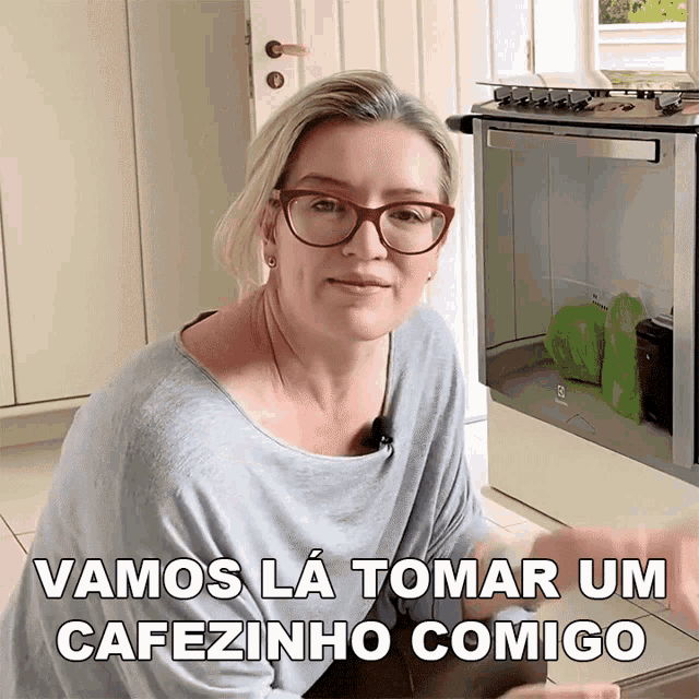 a woman wearing glasses stands in front of a stove with the words " vamos la tomar um cafezinho comigo " above her
