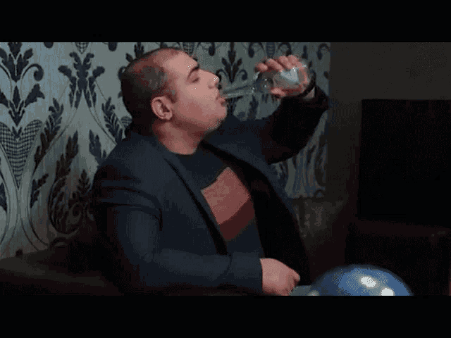 a man in a suit is sitting on a couch with a glass of wine .