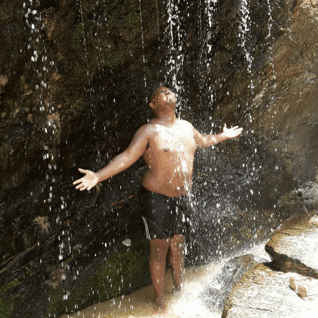 a shirtless man is standing in front of a waterfall with his arms outstretched