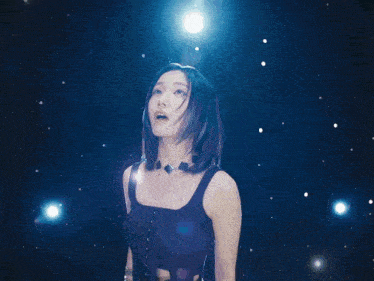 a woman in a black tank top stands in front of a dark background