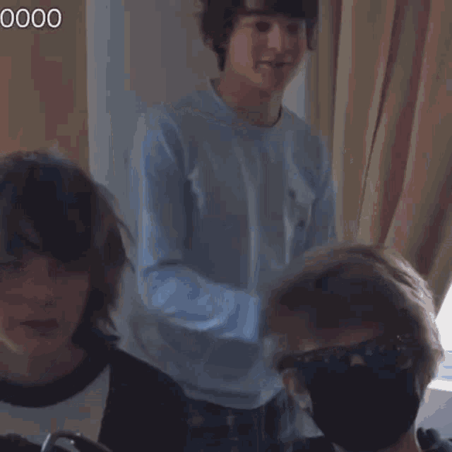 a man wearing a face mask and sunglasses is sitting next to another man .
