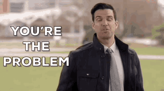 a man in a suit and tie is saying `` you 're the problem '' while standing in a field .