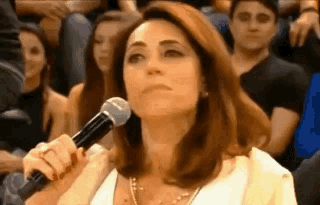 a woman is holding a microphone in front of a crowd of people in a theater .
