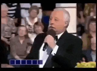 a man in a suit is speaking into a microphone in front of a crowd .