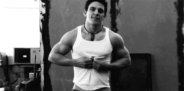 a black and white photo of a man in a white tank top taking off his shirt .
