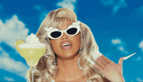a blonde woman wearing sunglasses holds a margarita with whipped cream on top