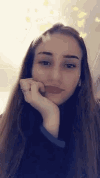 a woman with long hair and a ring on her finger is looking at the camera with her hand on her chin .