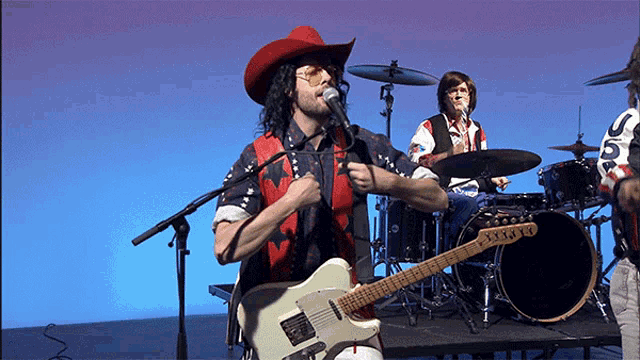 a man in a red cowboy hat is singing into a microphone while playing a guitar