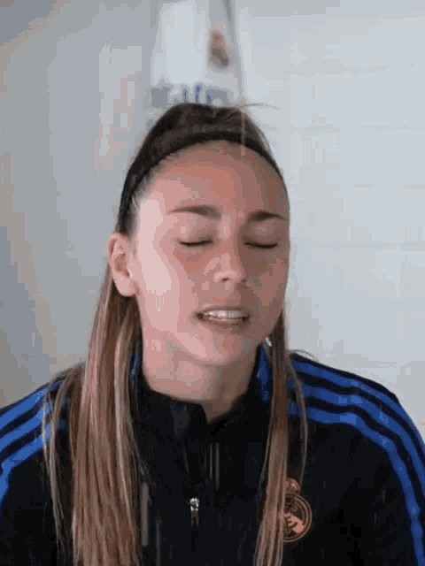 a woman wearing a headband and a real madrid jacket is making a face .