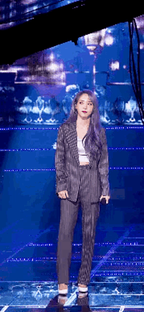 a woman with purple hair is standing on a stage wearing a suit and holding a microphone .