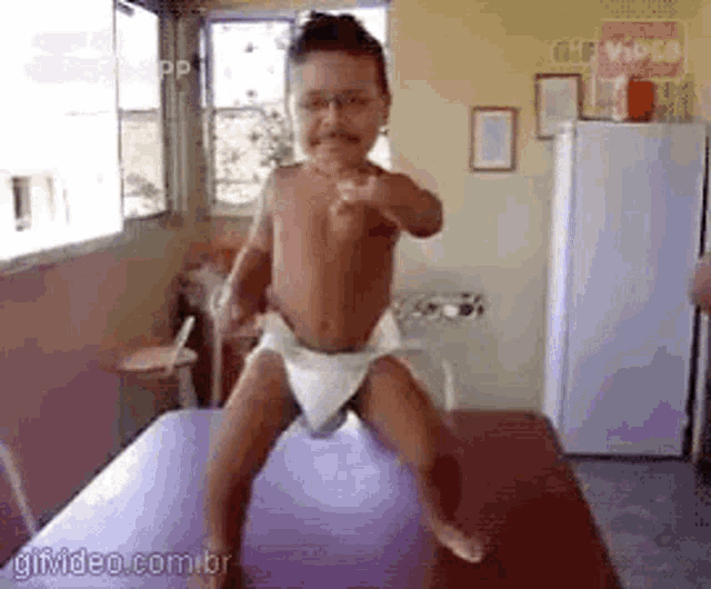 a baby in a diaper is standing on a table and pointing .
