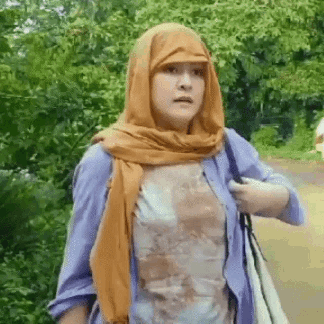 a woman wearing a scarf around her head and a purple shirt is walking down a road .