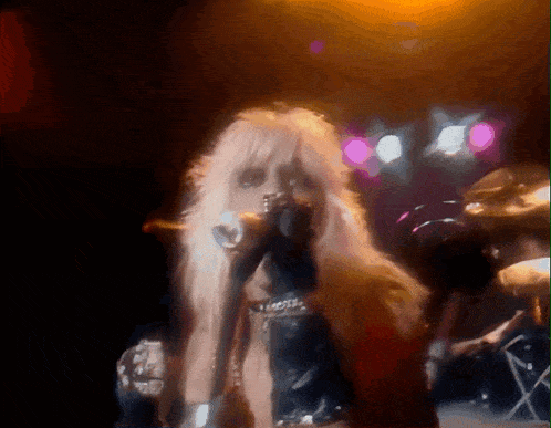 a woman with long blonde hair is singing into a microphone on a stage