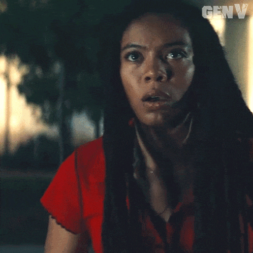 a woman with long black hair and dreadlocks is wearing a red shirt and a necklace .
