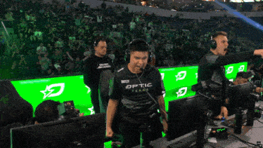 a man wearing a shirt that says optic stands in front of a crowd