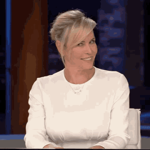 a woman in a white shirt is sitting at a table and smiling