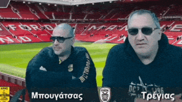 two men wearing sunglasses are sitting in front of a soccer field with the word ford on it