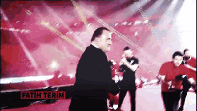 a man in a black suit stands in front of a red background that says fatih terim on it