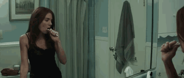 a woman is brushing her teeth in front of a bathroom mirror