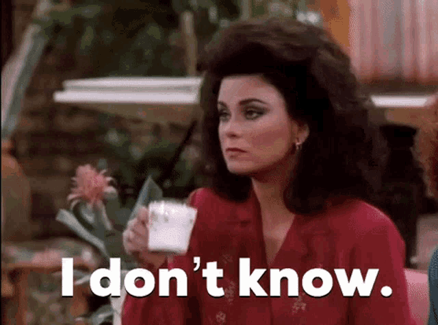 a woman is sitting at a table holding a cup of coffee and saying i don 't know .
