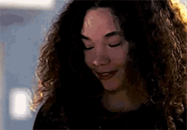 a woman with curly hair is smiling with her eyes closed and looking down .