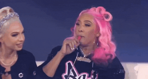 two women with pink hair are sitting next to each other and one of them is licking her lips .