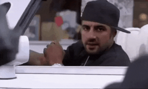 a man wearing a hat is sitting in a car and looking out the window .
