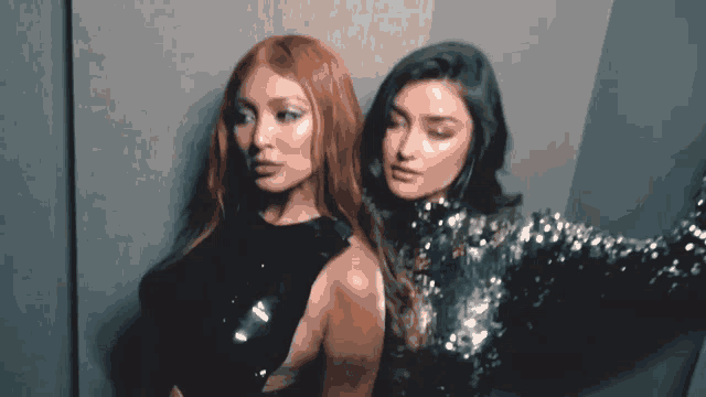 two women are standing next to each other in a room . one of the women has red hair .