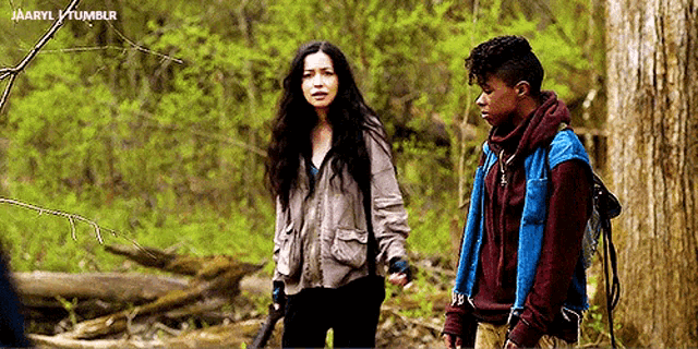 a man and a woman are standing in the woods holding guns .
