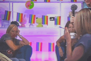 a group of people sitting in front of a shelf with rainbow flags on it