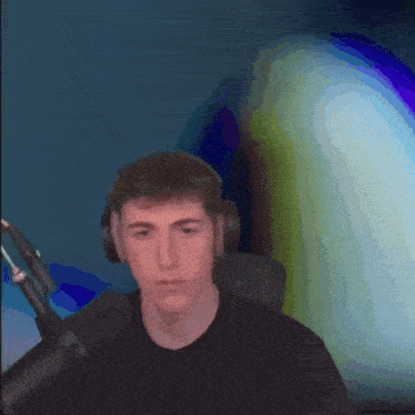 a young man wearing headphones and a black shirt is standing in front of a microphone .