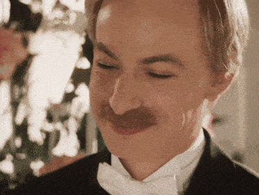 a man with a mustache wearing a tuxedo and bow tie smiles