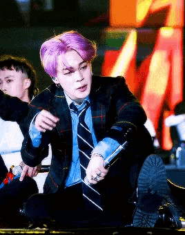 a man with purple hair is singing into a microphone on stage