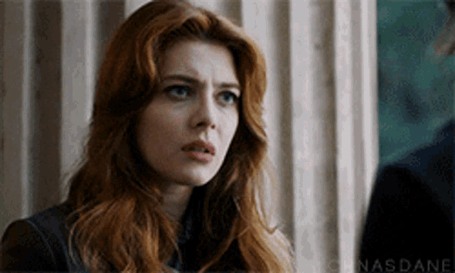 a woman with red hair and blue eyes is looking at the camera
