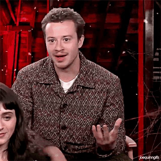 a man in a sweater is sitting in front of a woman and making a funny face